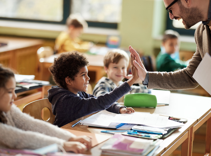 Happy teacher and schoolboy giving each other high-five on a class. stock photo